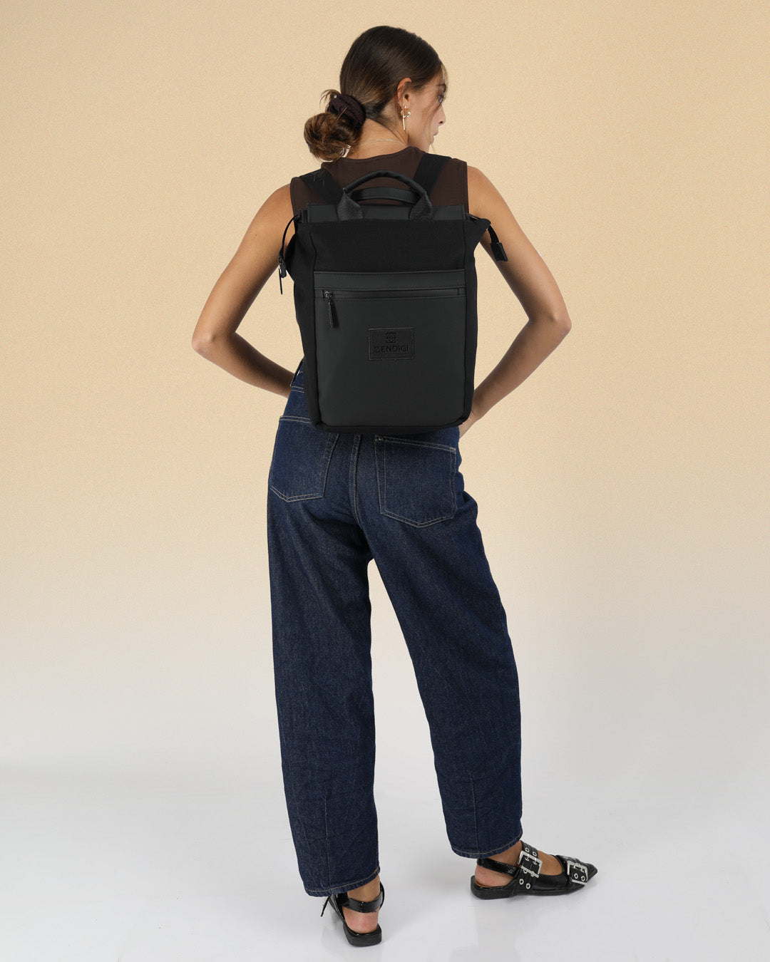 תיק גב למחשב שחור קנבס, תיק לפטופ ללימודים באוניברסיטה, תיק לסטודנטים, על דוגמנית עם רצועה אחת על הכתף, ניתן לראות את הפרופורציות של התיק על הדוגמנית