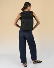 תיק גב למחשב שחור קנבס, תיק לפטופ ללימודים באוניברסיטה, תיק לסטודנטים, על דוגמנית עם רצועה אחת על הכתף, ניתן לראות את הפרופורציות של התיק על הדוגמנית