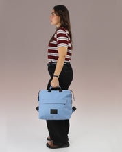 תיק גב מדריד כחול, מוחזק ביד על דוגמנית, ניתן לראות את גודלו באופן פרופורציונלי לדוגמנית, תיק גב שחור למחשב, תיק לנשיאה בידיים.