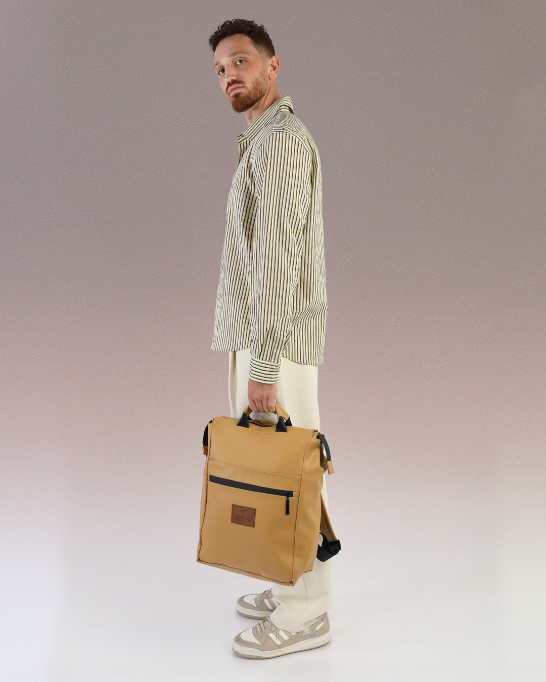 תיק גב למחשב קאמל לגבר, תיק לפטופ ללימודים באוניברסיטה, תיק לסטודנטים, על דוגמן מוחזק בידיות הנשיאה, ניתן לראות את הפרופורציות של התיק על הדוגמן.